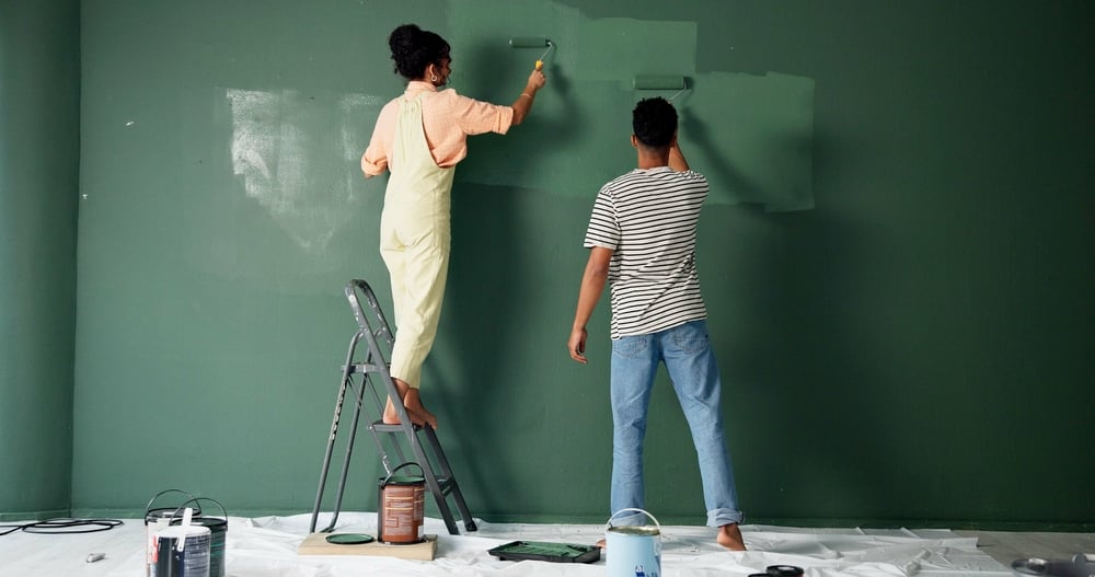 A couple painting a dark green wall together as part of a home improvement project, illustrating the '30% rule of renovation'—where small upgrades like paint can make a significant visual impact without exceeding 30% of the renovation budget.