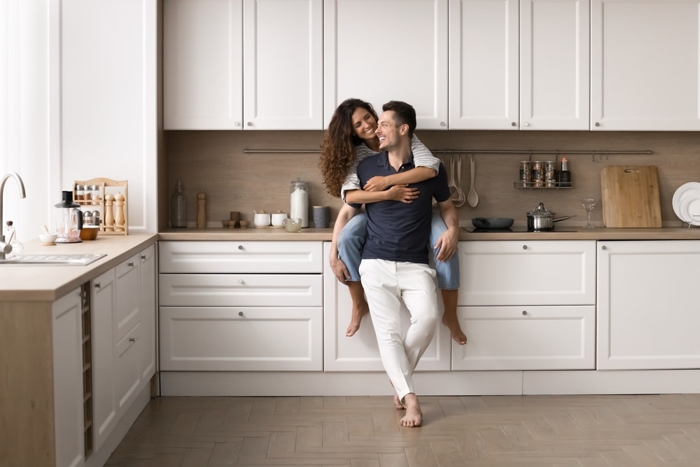 Happy couple embracing in a modern white kitchen with wooden accents, illustrating cozy design and smart home renovation tips for creating a functional and inviting space.