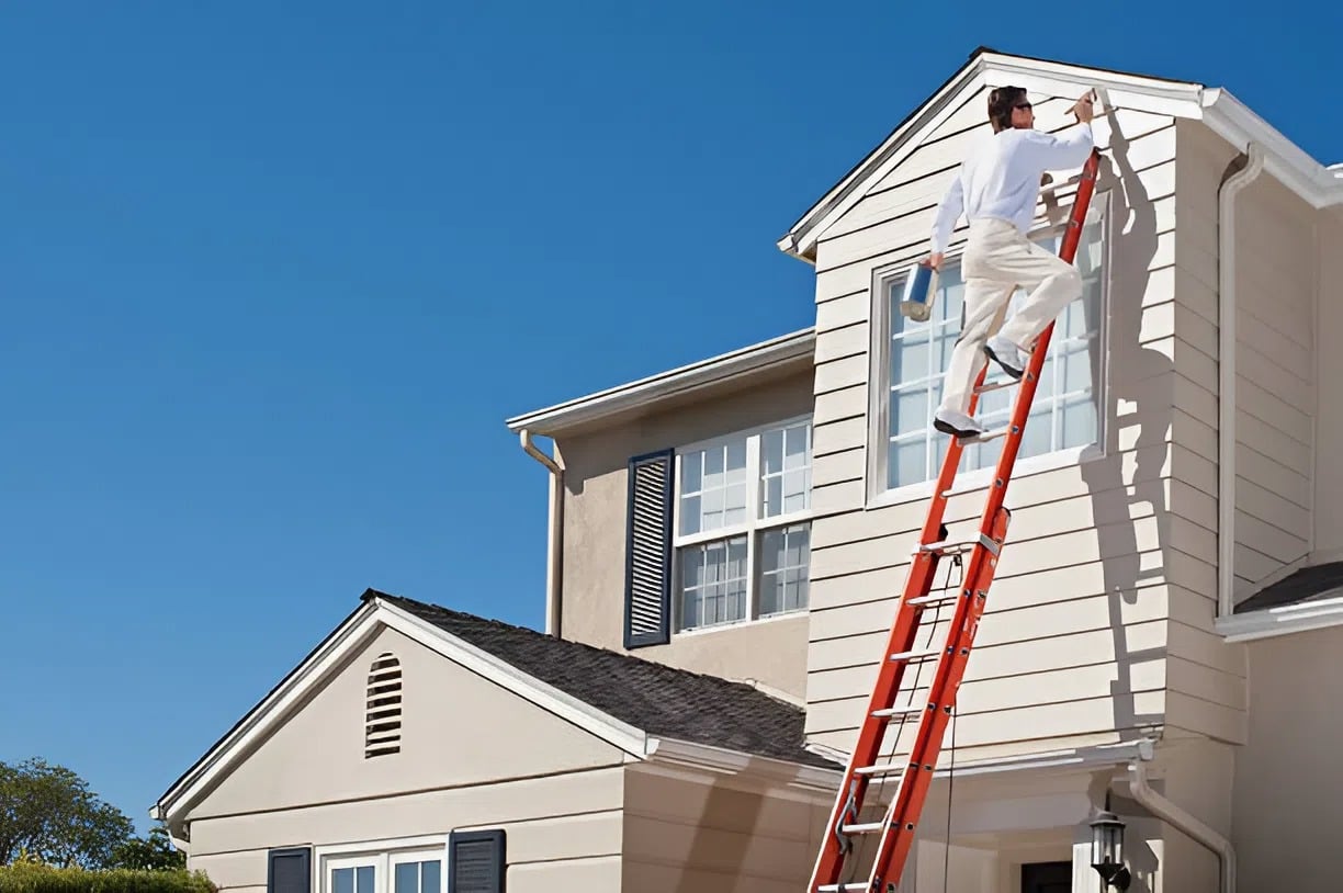 Exterior house painter in Wichita, KS, applying fresh light beige paint to a two-story home