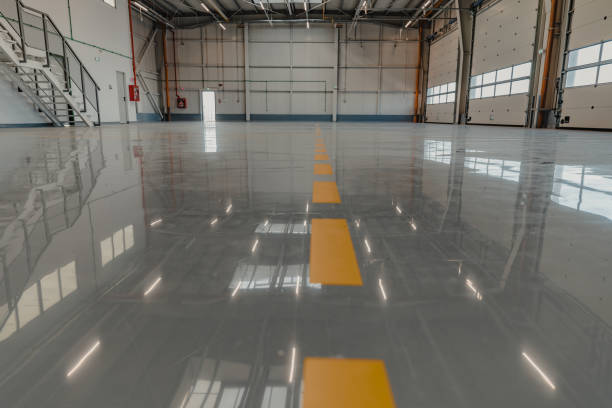Glossy gray epoxy-coated industrial warehouse floor with yellow safety line markings by a painting company in Valley Center, KS.