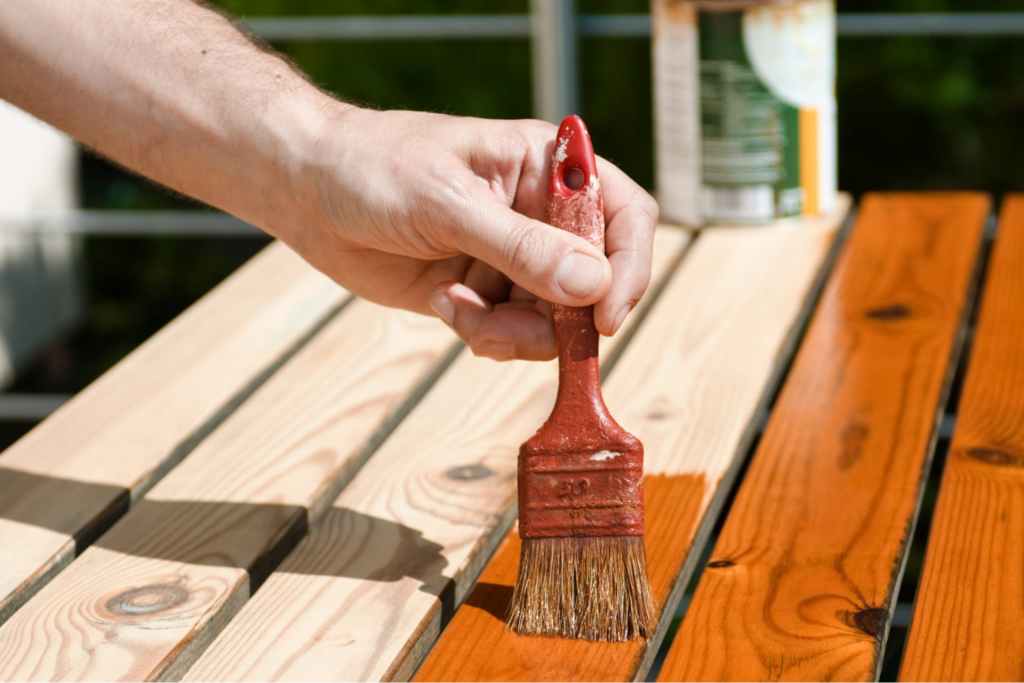 A professional applying a rich cedar stain to exterior wood decking for long-lasting protection by a painting company in Newton, KS.